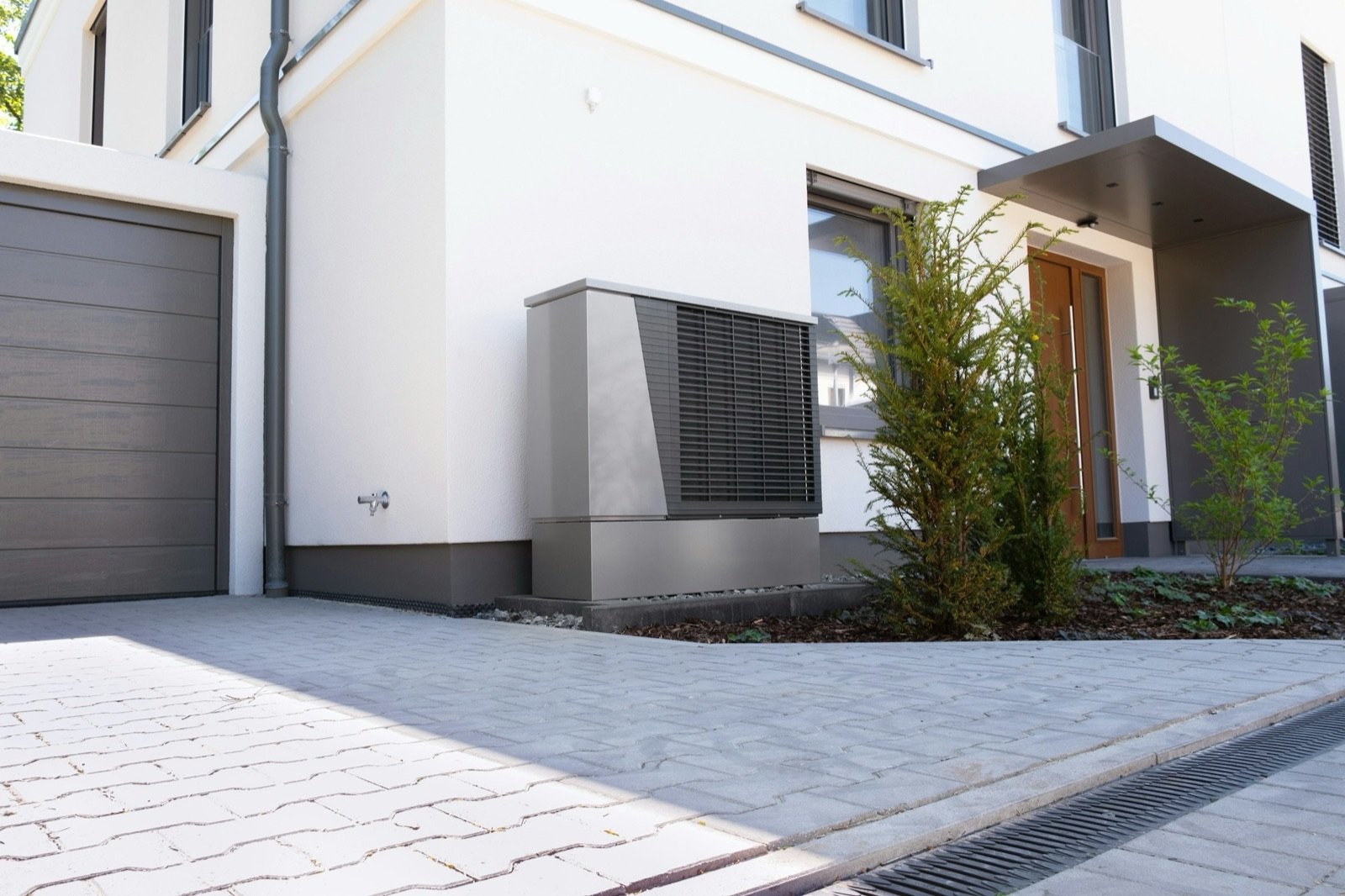 Pompe à chaleur air/eau posée contre la façade d'une maison, le long de l'allée